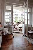 Gemütlicher Sessel in Zimmerecke, Blick auf den Balkon mit Tisch, Stühlen und Pflanzentöpfen