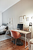 Multifunktionales Zimmer: Schreibtisch und Schalenstuhl vor grauer Wand, im Hintergrund Bett