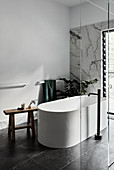 Free-standing bathtub and wooden stool behind glass wall