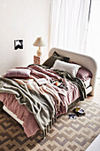 Bed with pillows and blankets in pink and green, marble pedestal with lamp