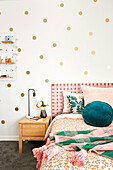 Bed with pink accents in front of wall with gold-coloured dots in the girls' room