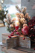 Kerze in Backförmchen auf Holzstern, Christbaumkugel, Tannenbäumchen und Hagebutten