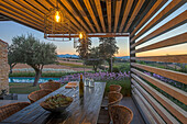 Esstisch mit Stühlen auf beleuchteter Terrasse mit Holz-Pergola