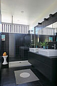 Black bathroom with washstand, twin sinks and shower area