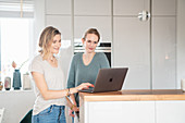 Two friends standing at the kitchen counter with laptop