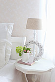 Weißer Kranz und Frühlingsblumen auf Nachttisch neben Bett