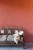 Wooden bench with tile inserts and cushions against brick-red wall