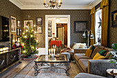 Illuminated Christmas tree in living room with vintage coffee table, sofa, and wallpaper