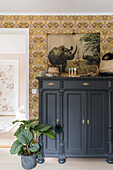 Grey lacquered chest of drawers, above it vintage poster with animal motif and floral wallpaper