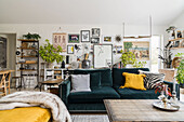 Petrol-colored sofa with cushions, behind it picture gallery and shelves in living room