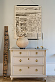 Old poster with a map above chest of drawers with vase and candle holder