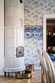 White tiled stove in room with patterned wallpaper and blue and white wall mounted plates