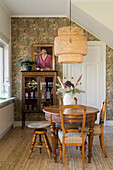 Round antique table with chairs in the dining room with patterned wallpaper