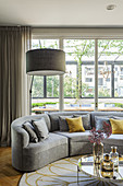 Grey, curved sofa with scatter cushions in front of window