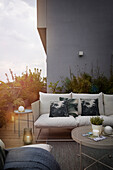 Sofa with white cushion and throw pillows and a round outdoor coffee table on the terrace