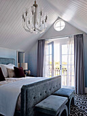Doppelbett und Hocker mit blau-grauem Bezug in elegantem Schlafzimmer mit Balkon