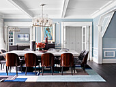 Dining table with marble top and designer chairs in open plan living room with white coffered ceiling and light blue walls