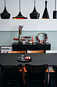 Schwarzer Esstisch, darüber schwarze Pendelleuchten, im Hintergrund Konsole mit Blumenkränzen