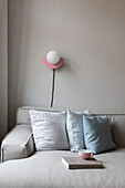Pink wall-mounted lamp above light grey sofa with scatter cushions