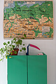 Green cupboard with house plant and table lamp on top below map on wall
