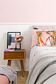 Retro bedside table next to a bed in bedroom with white and pink wall