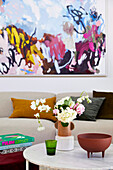 Blick über Marmor-Coffeetable mit Blume auf Sofa mit Kissen, darüber Kunstwerk