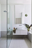 Duschbereich mit Glasscheibe, Waschtisch aus Carrara-Marmor mit Doppelwaschbecken und weiße Wandfliesen im Badezimmer