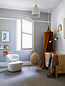 Weißer Sessel, Stehlampe und Babybett mit Baldachin im Zimmer mit grauer Wand