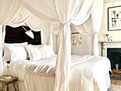 Bett mit weißer Bettwäsche und Baldachin in gemütlichem Schlafzimmer