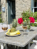 Weingläser, Ananas und Rosen auf Steintisch auf der Terrasse
