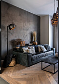Black sofa against concrete-look wall in living room with oak parquet floor