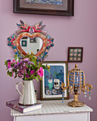 Vintage bedside table with flowers in a jug, painting, and lamp