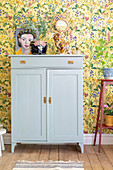 Grey cupboard with vintage ornaments against floral wall