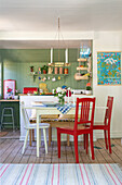 Red chairs around dining table in front of open-plan kitchen in Swedish style
