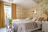 Double bed with silver-coloured bedspread and floral wallpaper in bedroom