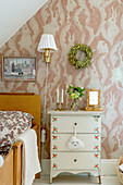 Wooden bed and shabby-chic chest of drawers in the girl's room with hare-patterned wallpaper