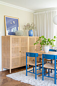 Half-high rattan cabinet and blue chairs around table in dining room