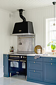 Blue base units and black cooker with extractor hood in kitchen with white-painted wood panelling