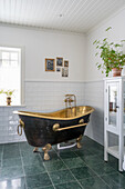 Freestanding brass bathtub in bathroom with green floor tiles