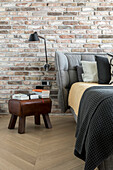 Bed with upholstered headboard against brick wall and retro stool with leather cover in bedroom