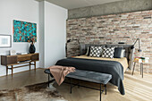 Double bed with upholstered headboard against brick wall, clothes bench and console table in bedroom