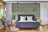 Queen bed in front of wallpapered wall, tree trunk bedside tables and rocking chair in a bedroom