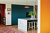 Kücheninsel mit Marmorverkleidung und petrolfarbene Einbauküche in offenem Wohnraum