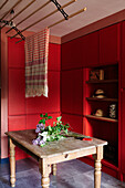 Rot lackierte Einbauten und alter Holztisch mit Fliedern