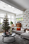 Round coffee table, Christmas tree, sofa and bureau in living room with patterned wallpaper