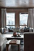Sofa with scatter cushions in front of windows in elegant living room with view over snowy landscape