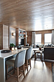Kitchen island with upholstered chairs and lounge in background in elegant interior with wood panelling