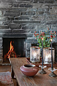 Blick über Holz-Couchtisch auf Natursteinkamin mit Feuer im Wohnzimmer
