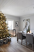 Illuminated Christmas tree, presents underneath and festively set dining table