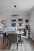 Round table with upholstered chairs and sideboard below gallery of photos on wall